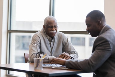 two people sitting at a table looking at a laptop