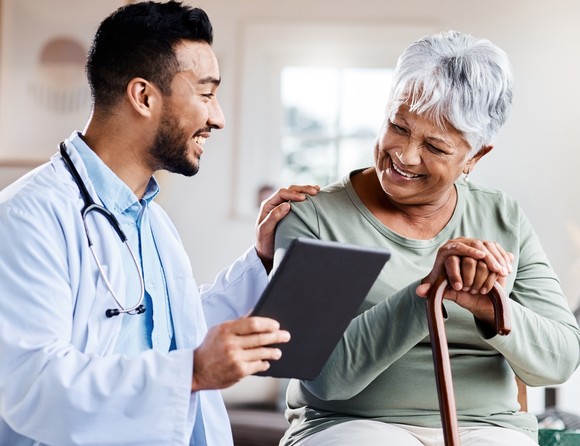 A young doctor shares information on a tablet with a senior patient with a cane.