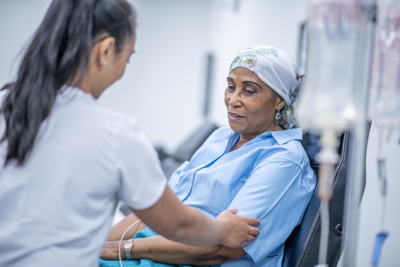 A woman in blue with a head scarf receives treatment from a female healthcare worker.