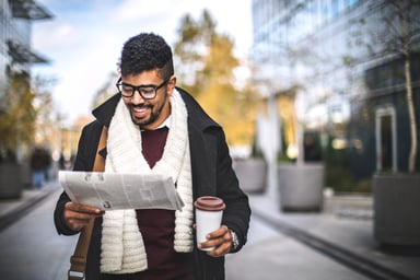 Man reading newspaper outside with coffee