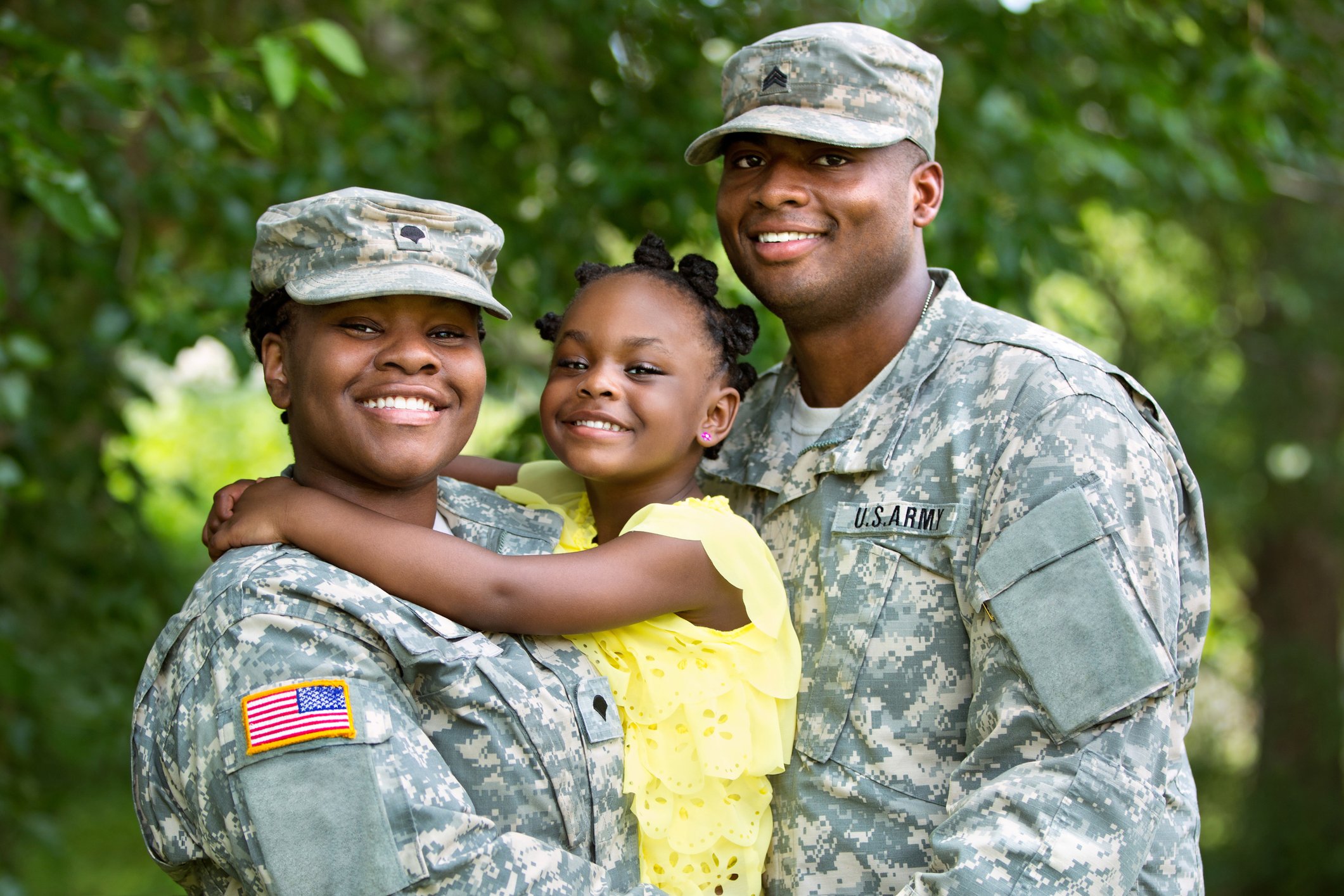 Two adults in military uniform smile with a child.