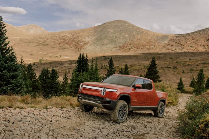 A red Rivian R1T pickup truck on a dirt road in the mountains. 