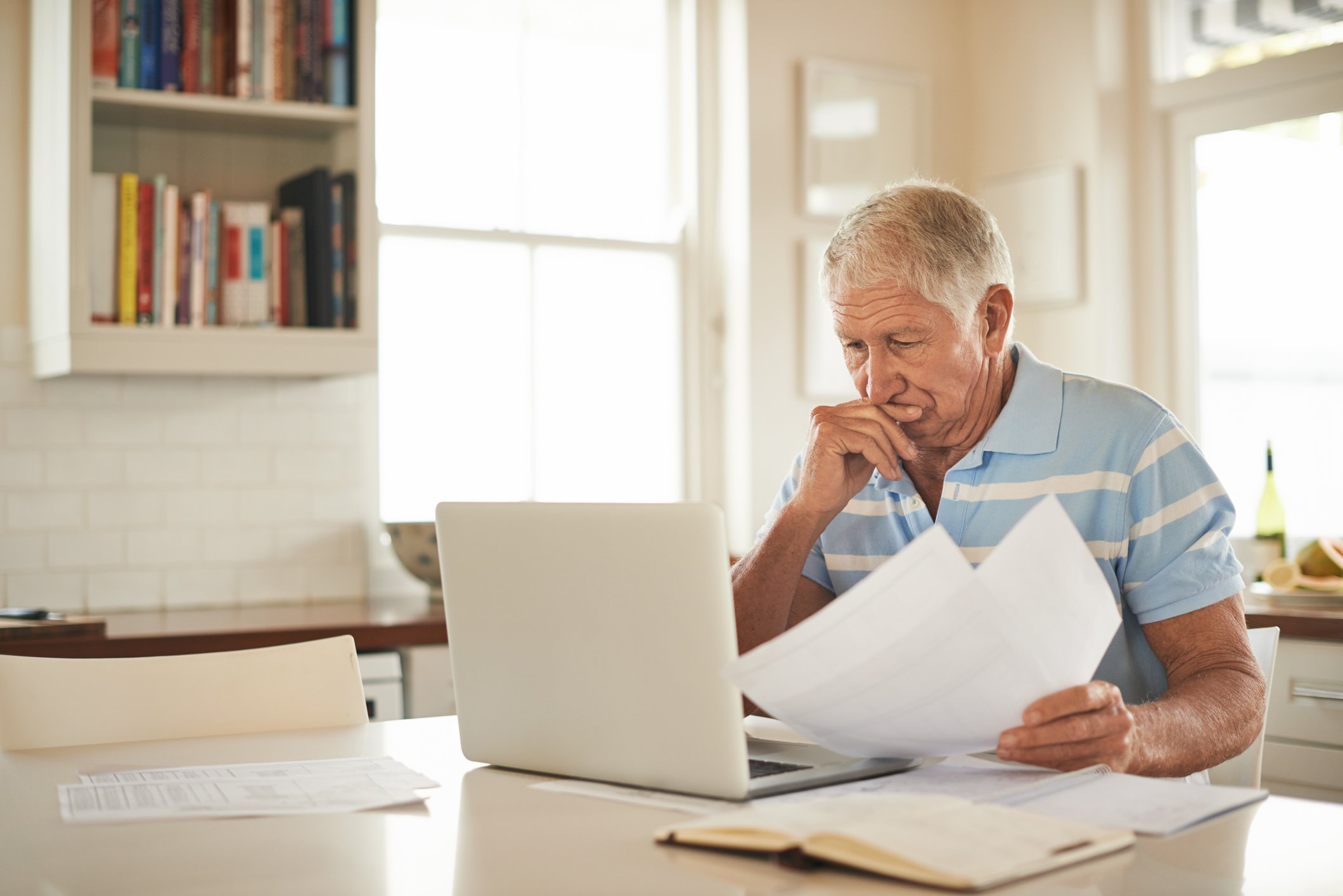 A person with a serious expression reading papers at a laptop.