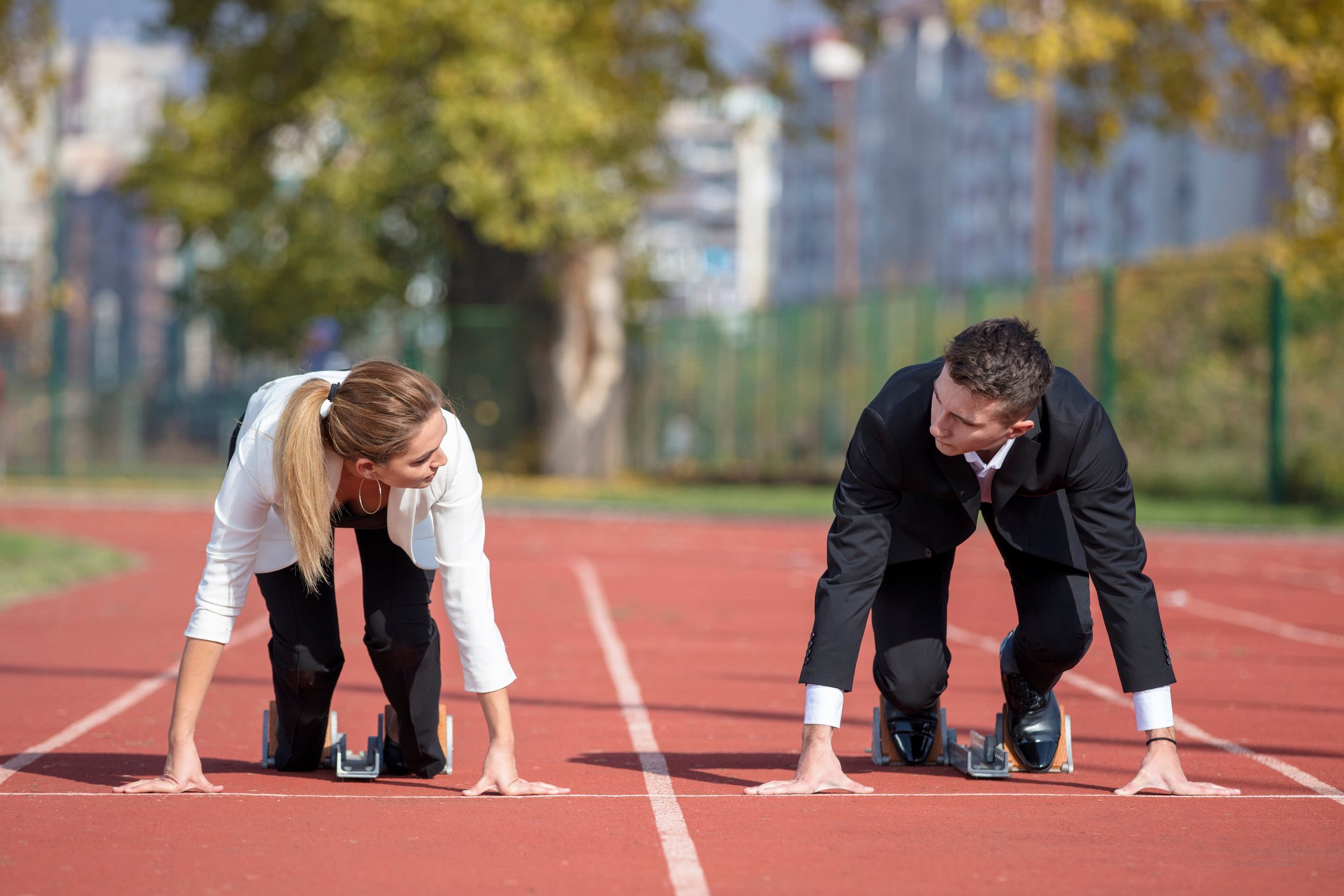 Two business people line up for a race on a running track.