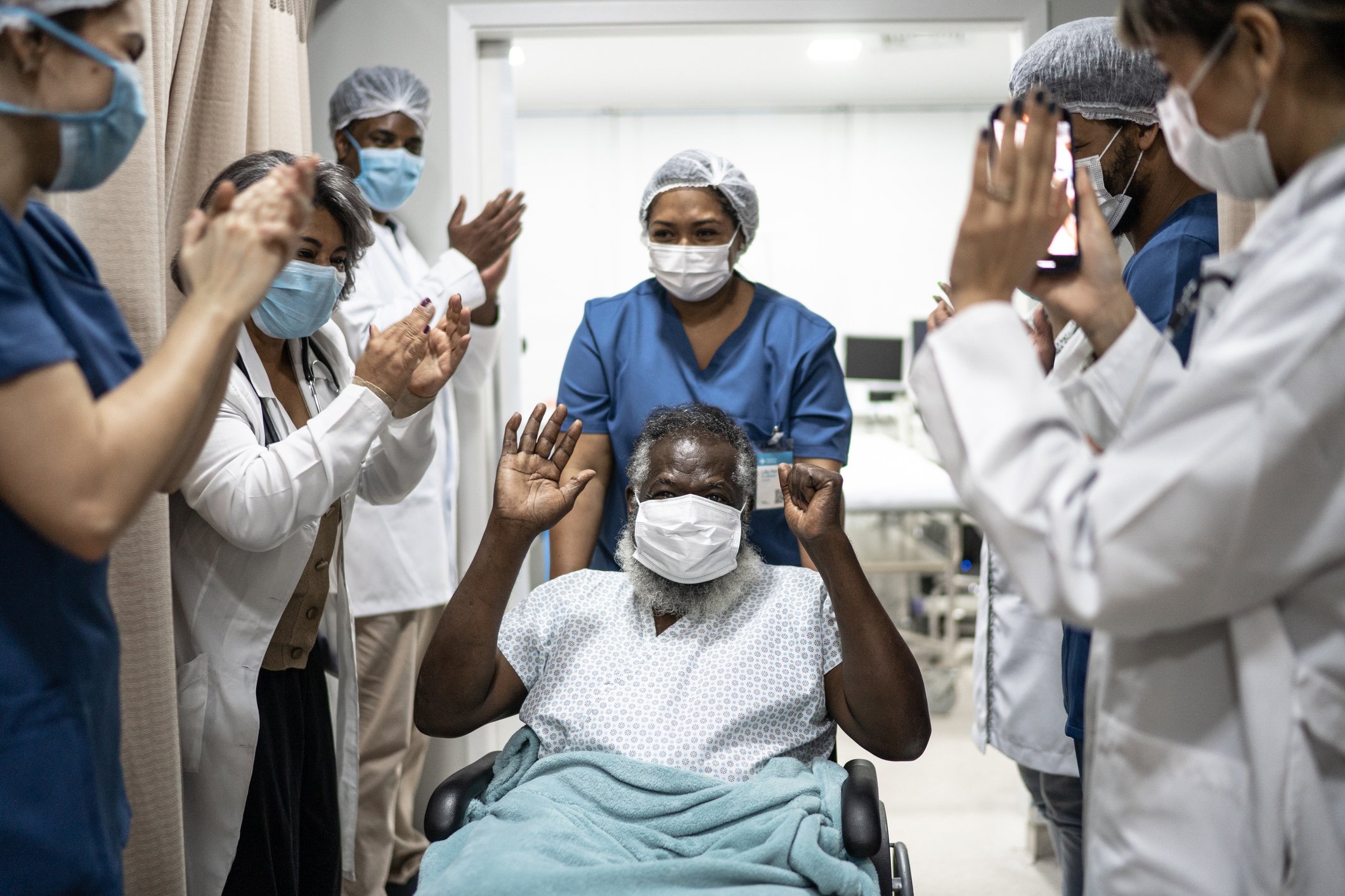 Medical professionals applauding a patient with hands raised.