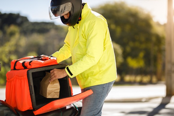 A delivery driving wearing a motorcycle helmet and grabbing a small brown bag.