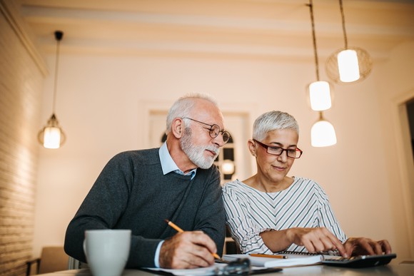 An older couple sitting at a table with a calculator and notebook.