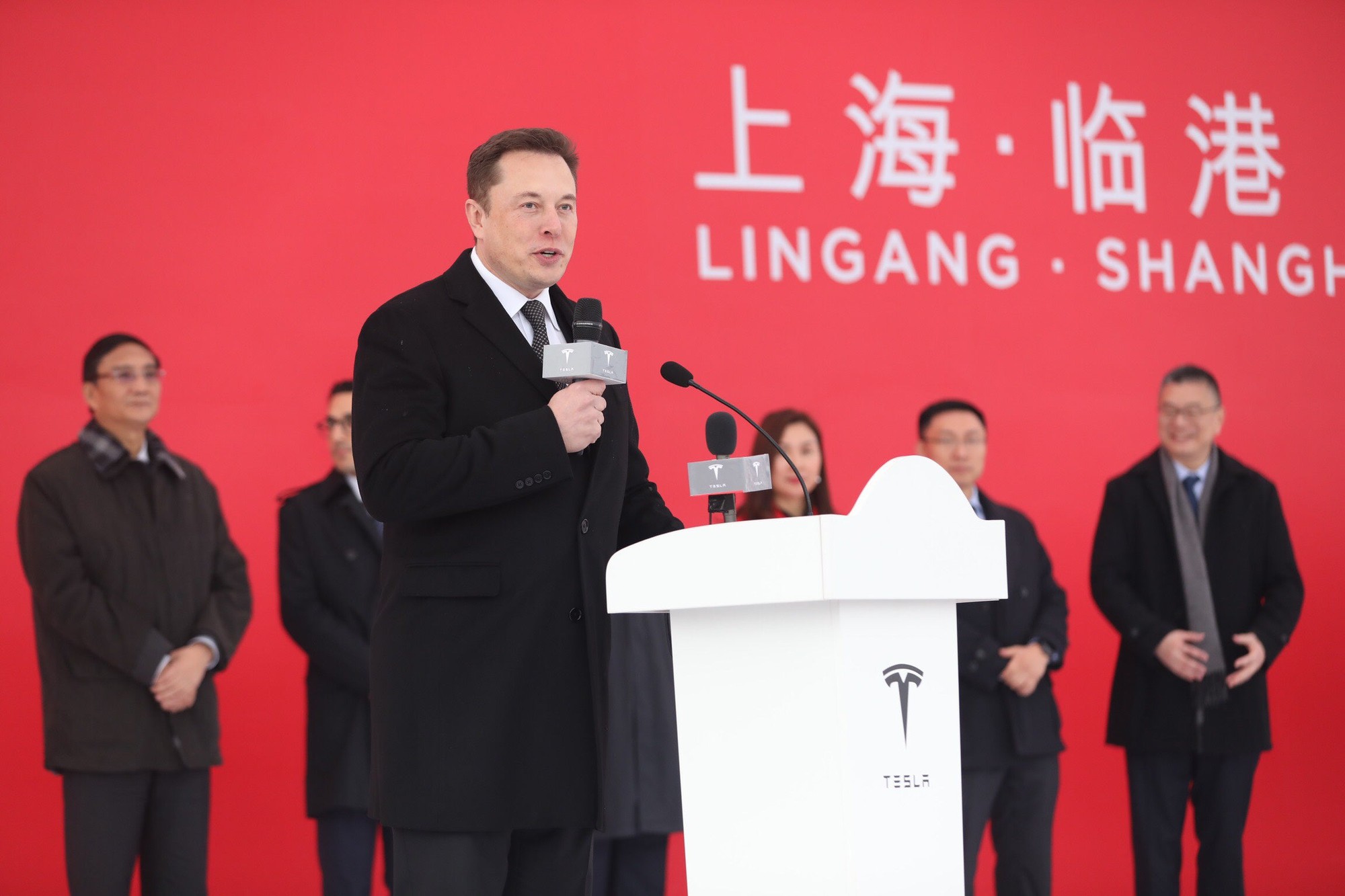 Tesla CEO Elon Musk speaking behind a podium at the Shanghai gigafactory groundbreaking ceremony.