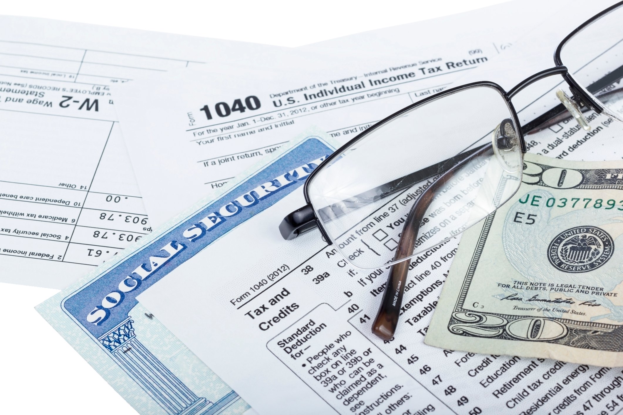 A Social Security card wedged between U.S. tax forms, with eyeglasses and a twenty-dollar bill set atop the tax forms.