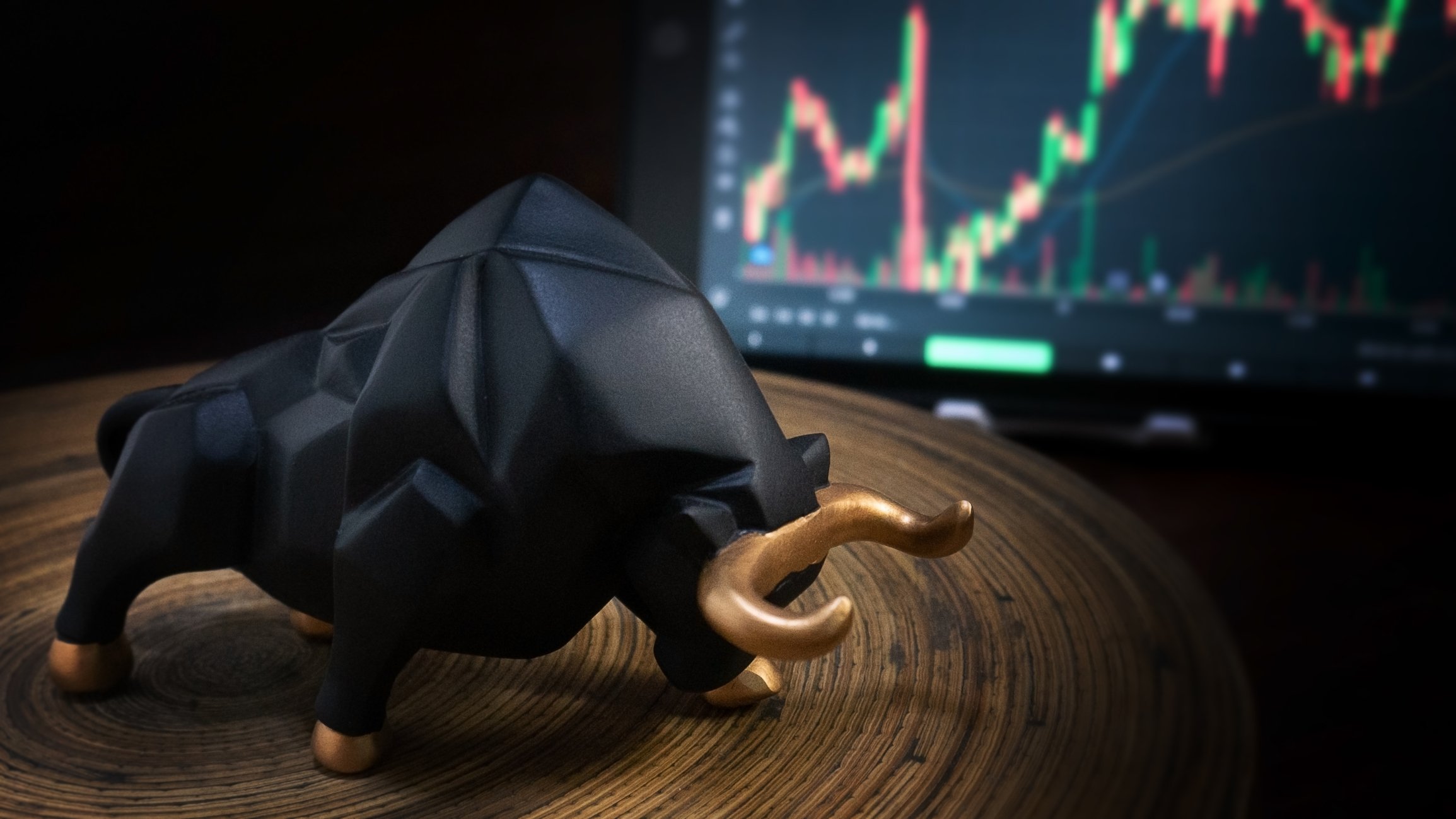 A figurine of a bull in front a trading screen.