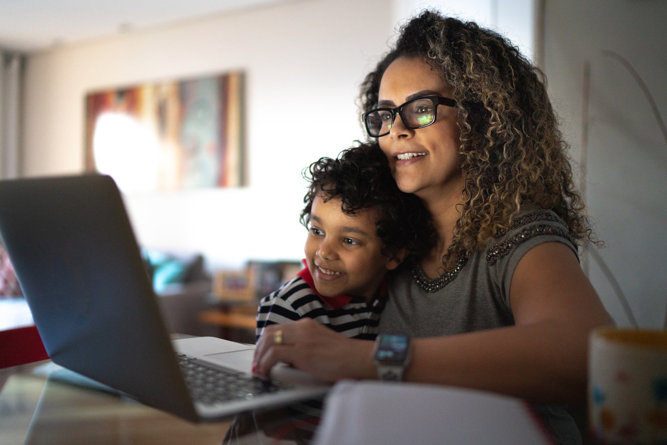 Smiling person with arm around child looking at laptop.