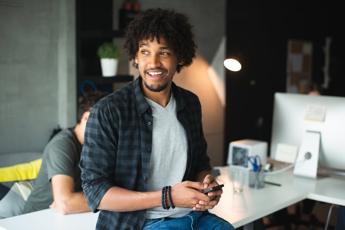 Young investor smiling while checking smartphone in an office.