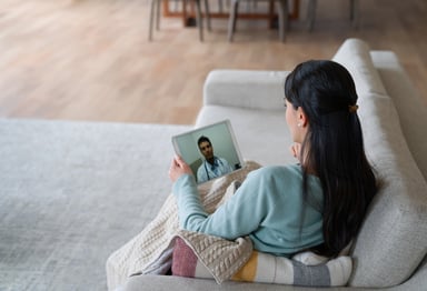 Woman on couch talking to doctor on tablet.