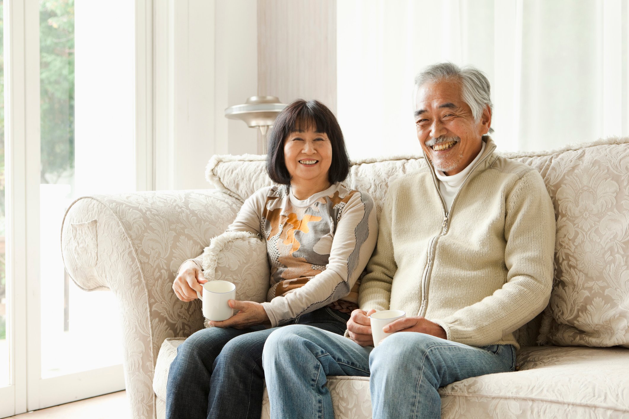 Smiling couple sits on couch at home, each holding a coffee mug.