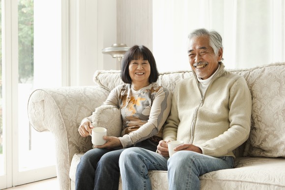 Smiling couple sits on couch at home, each holding a coffee mug.