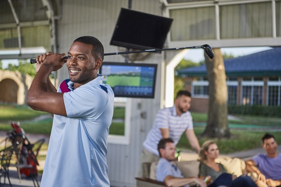 A golfer at Topgolf holds a golf club behind their back after a swing.