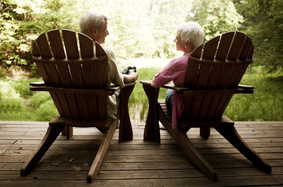 Two smiling seniors sitting on chairs out on deck.