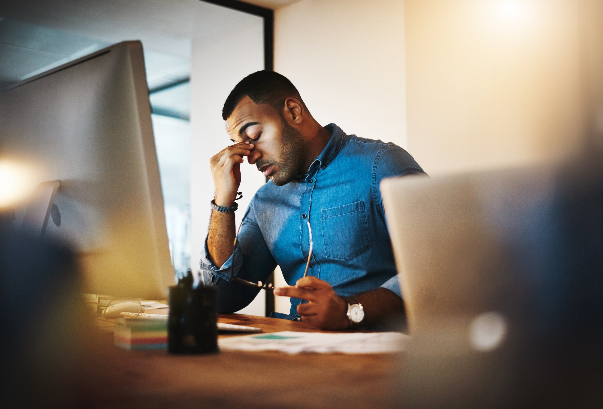 A person sits at a desk with holding the bridge of their nose in defeat.