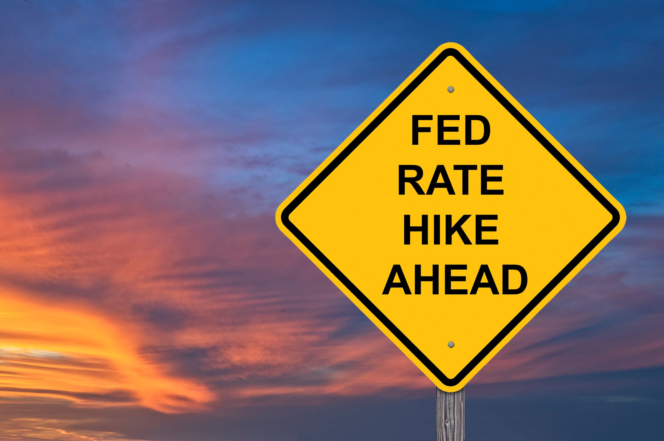 Street sign reading "Fed rate hike ahead" set against a cloudy sky at sunset.