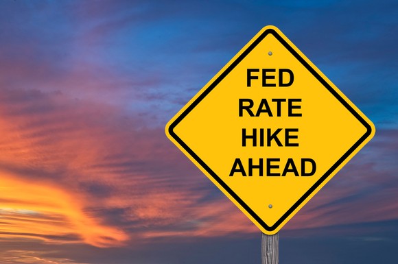 Street sign reading "Fed rate hike ahead" set against a cloudy sky at sunset.