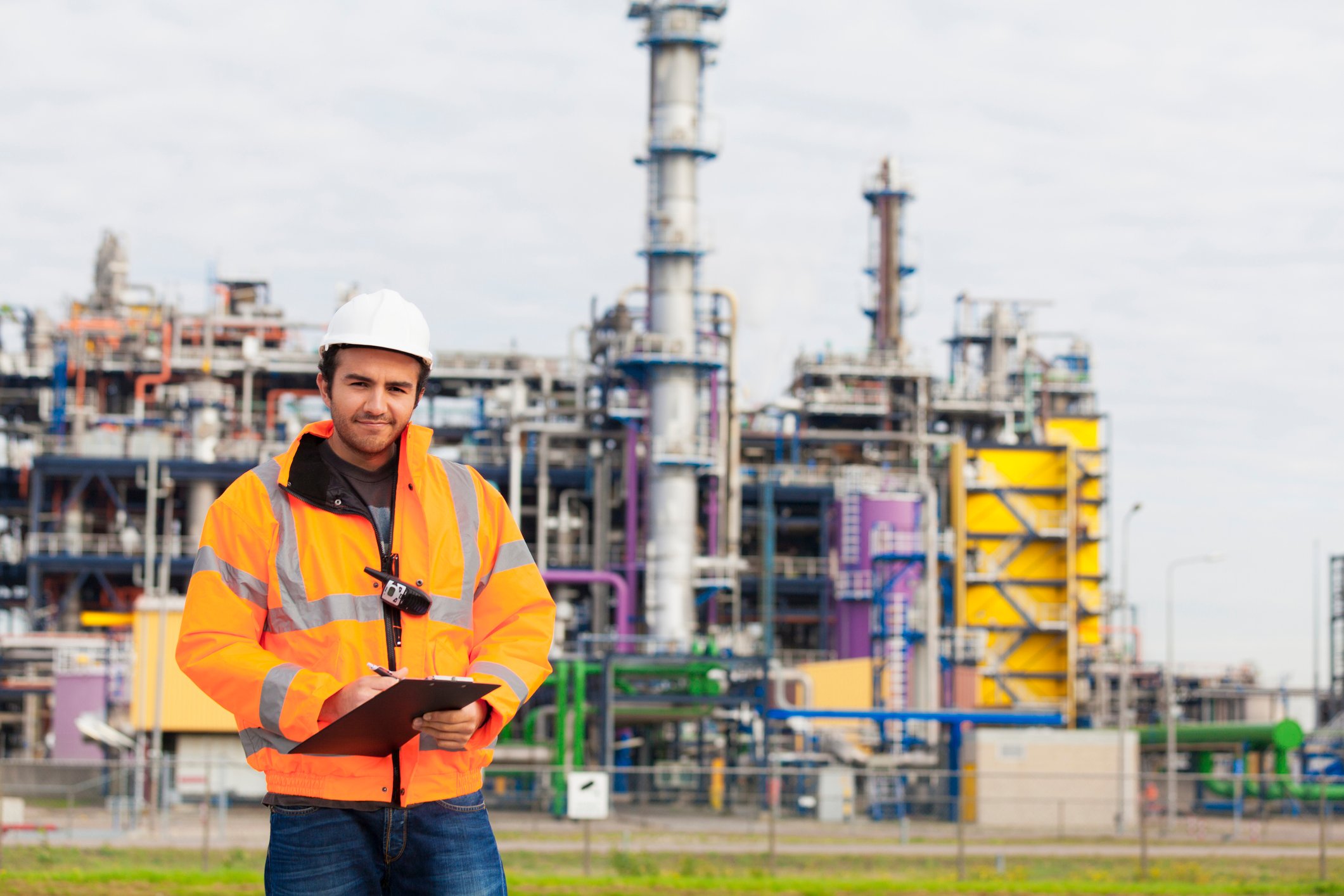 "A person wearing safety equipment stands outside a chemical plant."