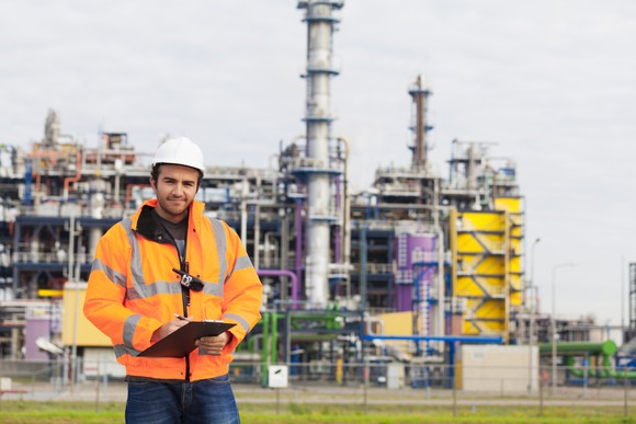 "A person wearing safety equipment stands outside a chemical plant."