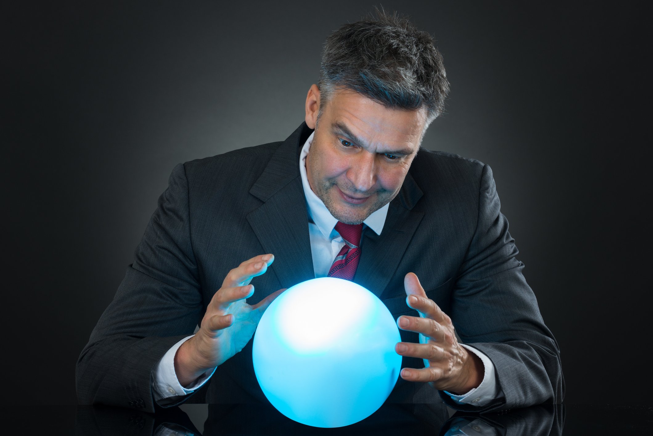 A businessman in a suit looks in a crystal ball.