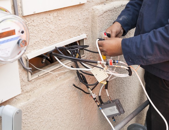 A technician works on coaxial cable connections outside a residence.