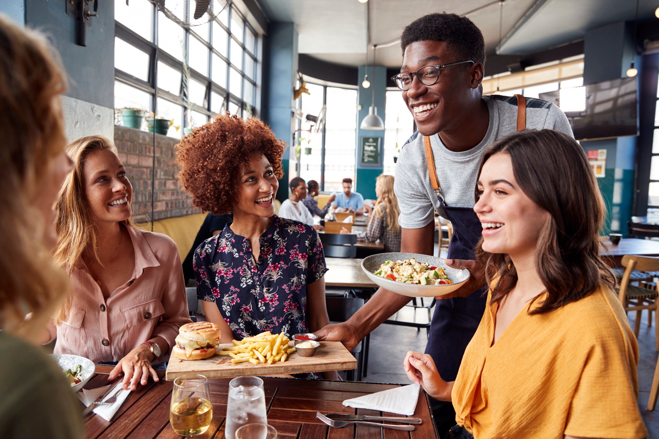 A server bring food to a table full of hungry restaurant patrons.
