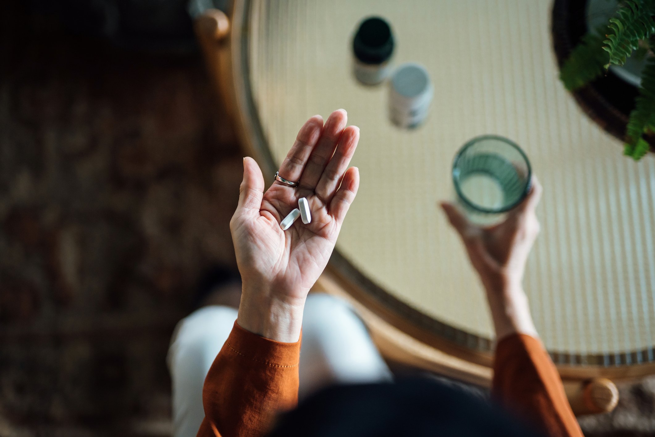 A person holding medicines in one hand and a glass of water in the other.