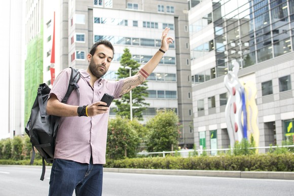 A person holding a phone and hailing a taxi.
