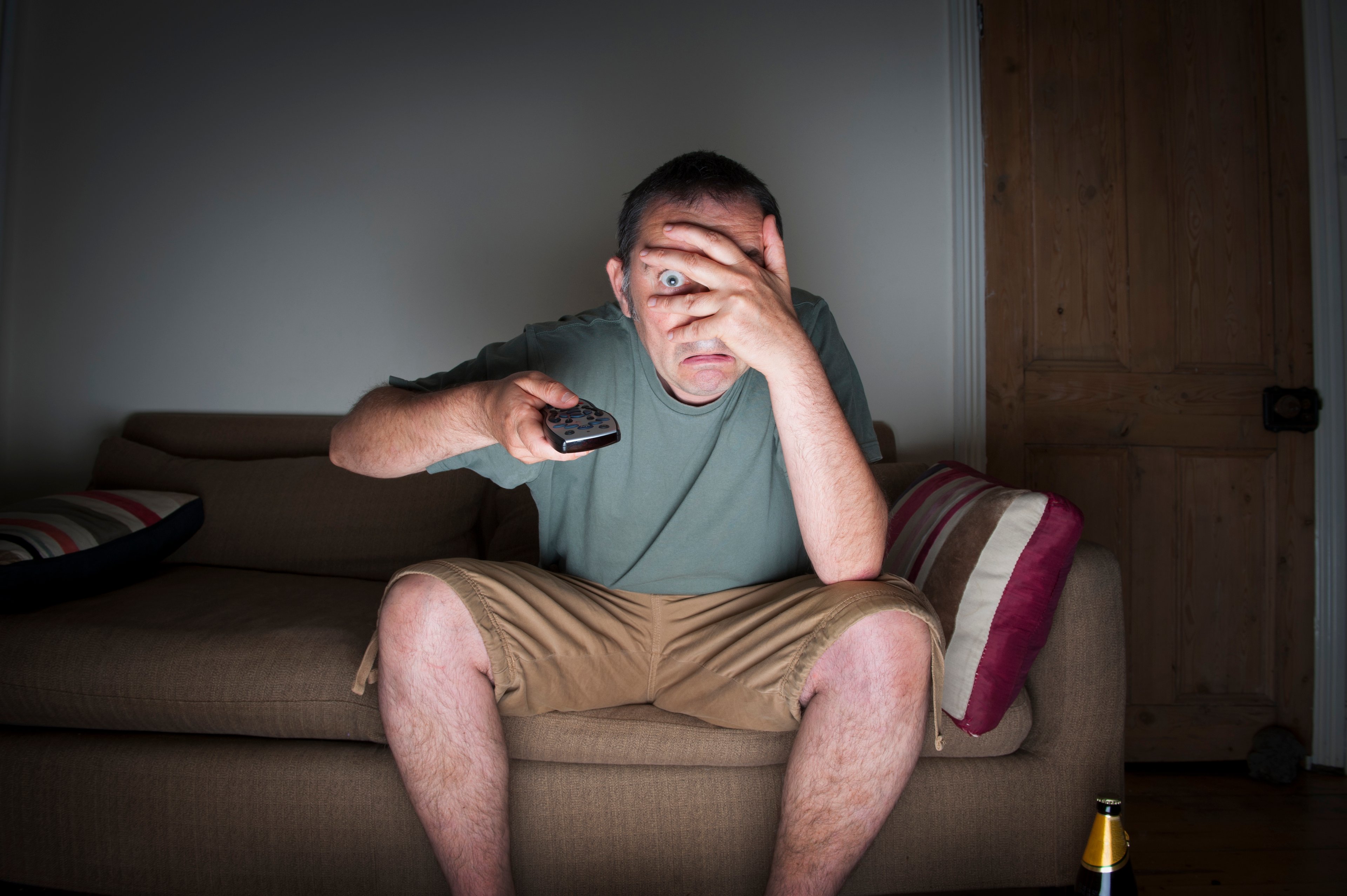 Man watching TV and covering eyes.