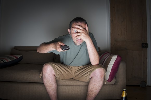 Man watching TV and covering eyes.