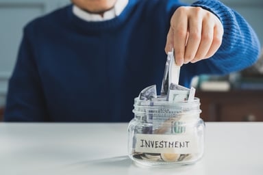 A person putting money in a jar for investment.