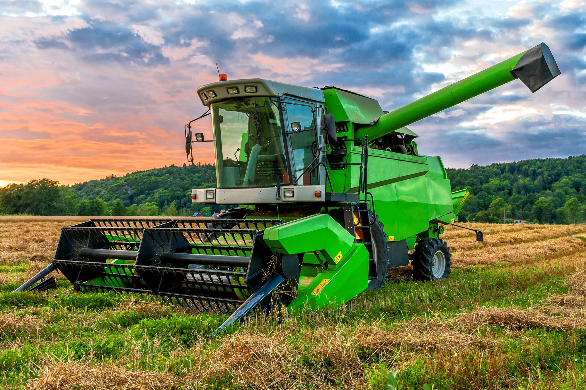 A green combine in a field at sunrise. 