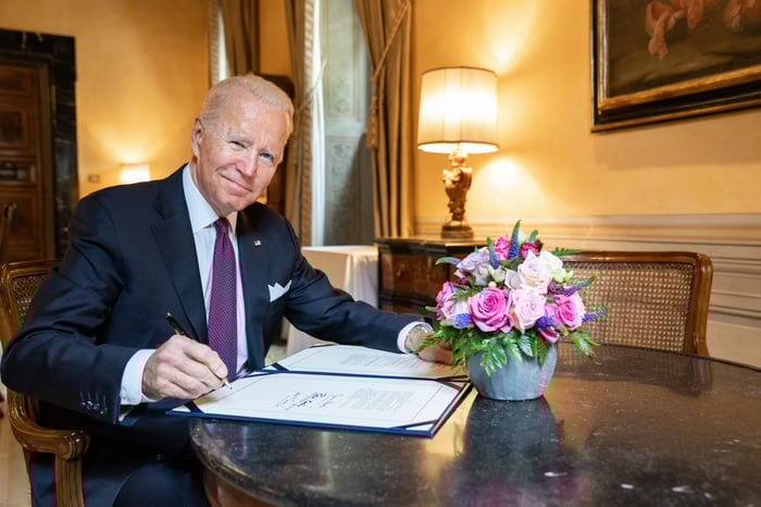 Joe Biden sitting a desk holding a pen over a document.