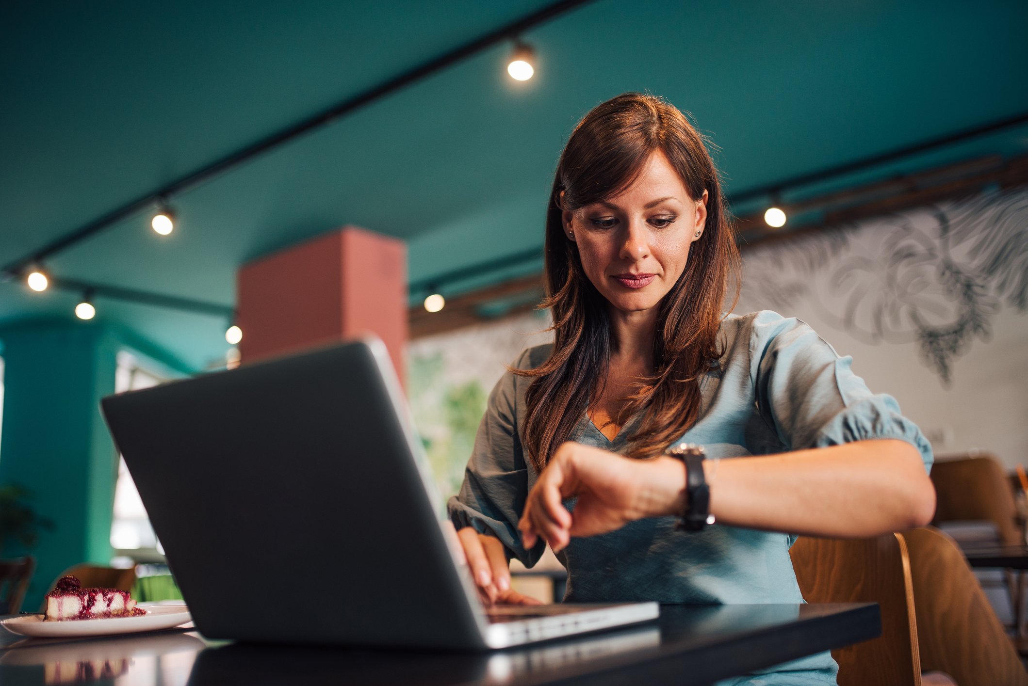 A person looking at a watch while sitting in front of a laptop.