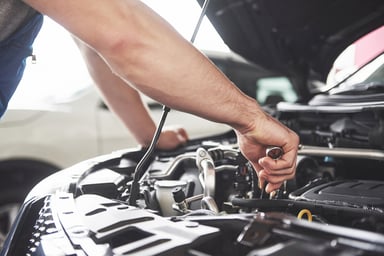 person works on car engine holding a wrench