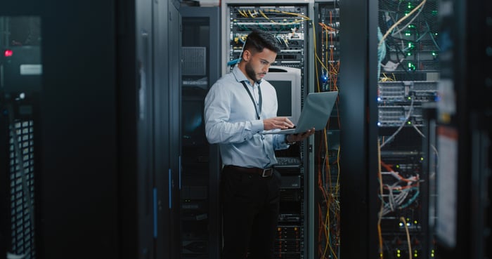 Network engineer in a data center looking at data on a laptop computer.