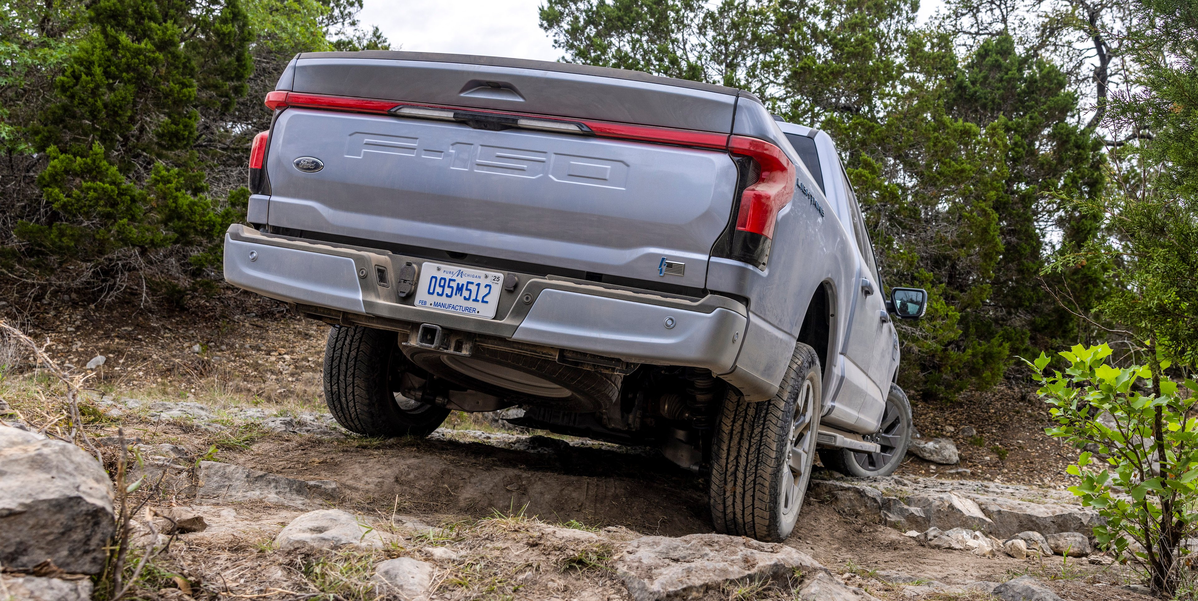 Rear view of Ford F-150 Lightning off-roading near several trees.