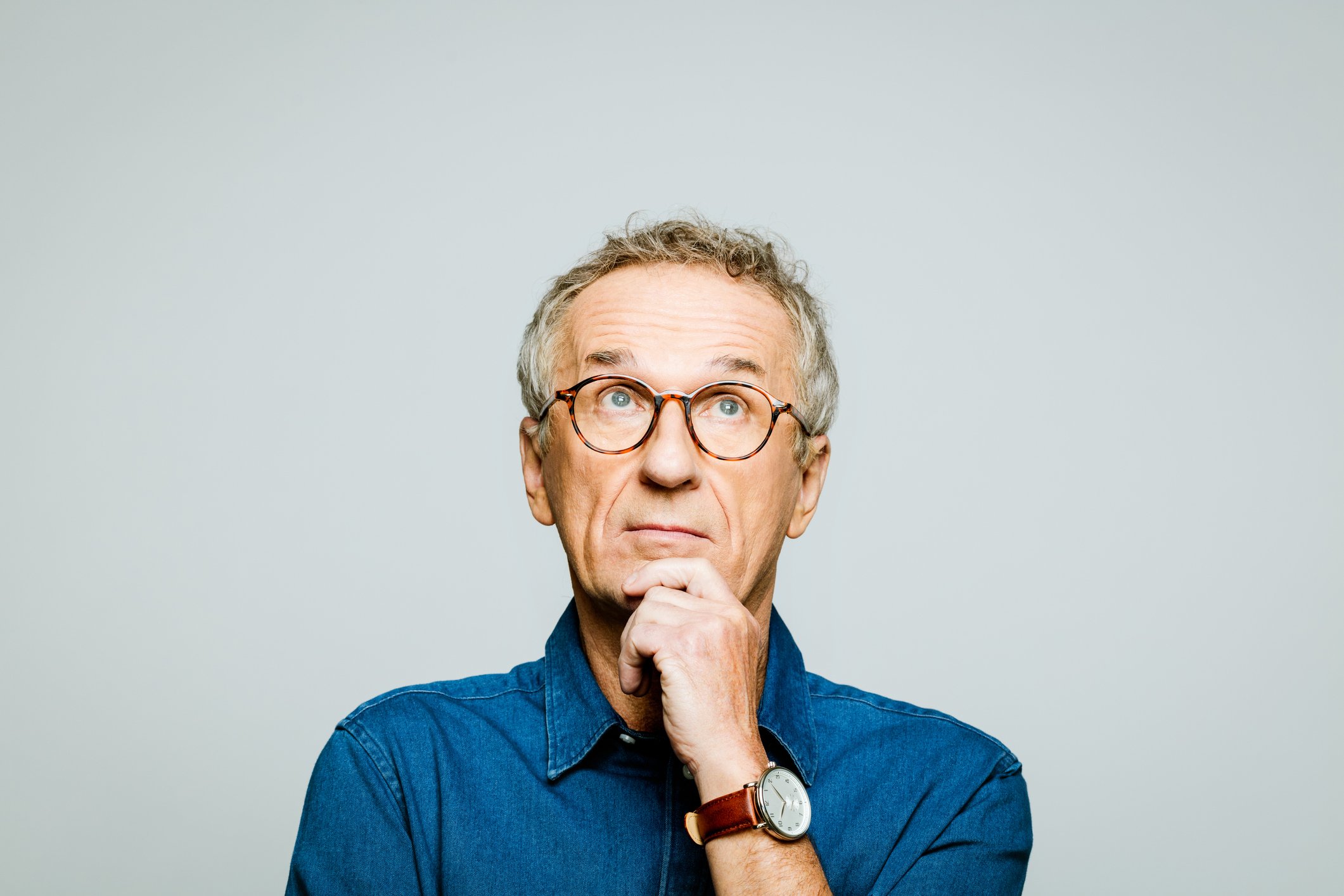 A person with glasses holds their chin on their hand while thinking.