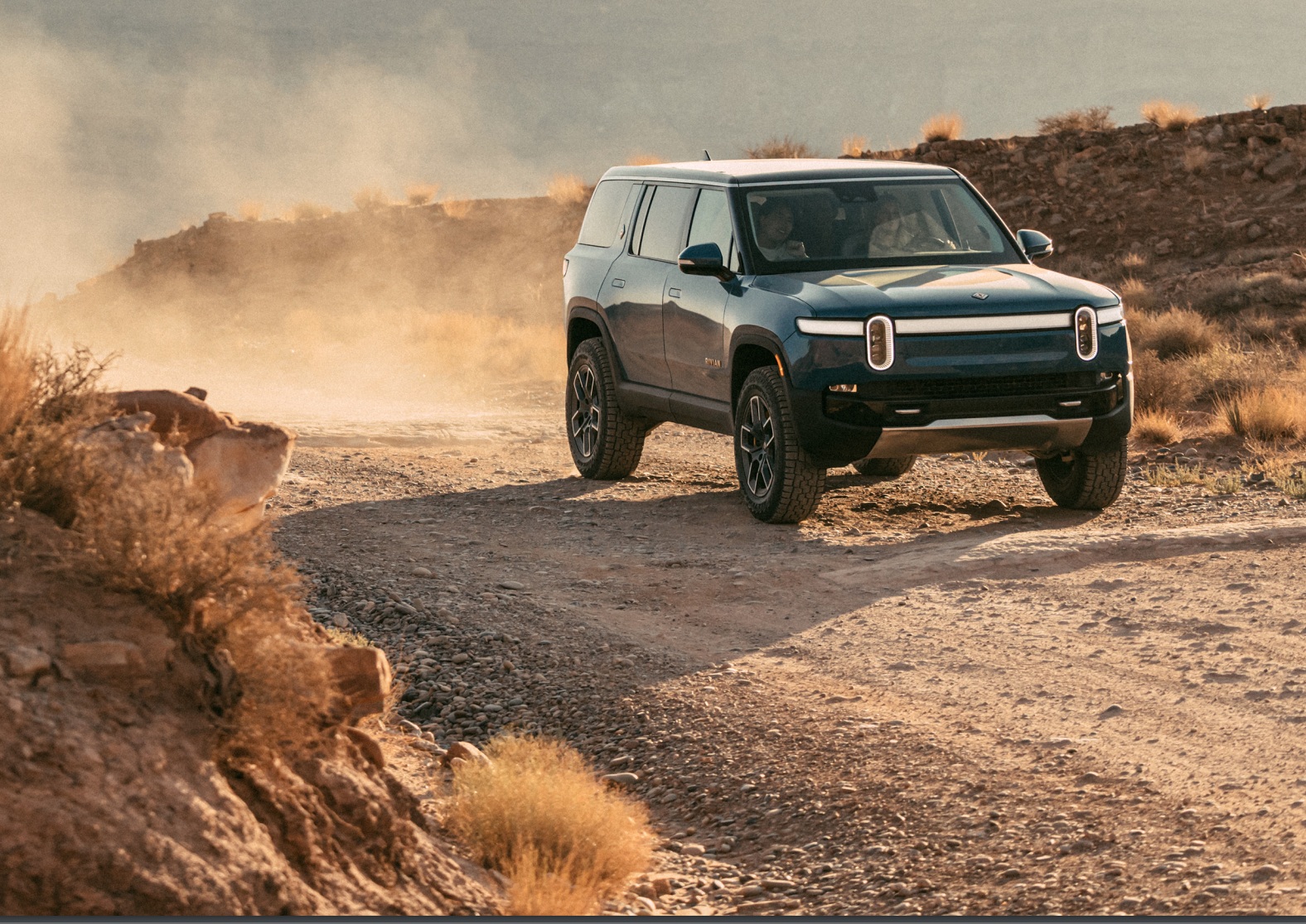 Rivian R1S electric SUV on dirt road. 