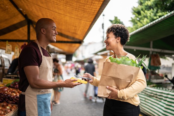A person uses a phone to make a purchase at a street market.