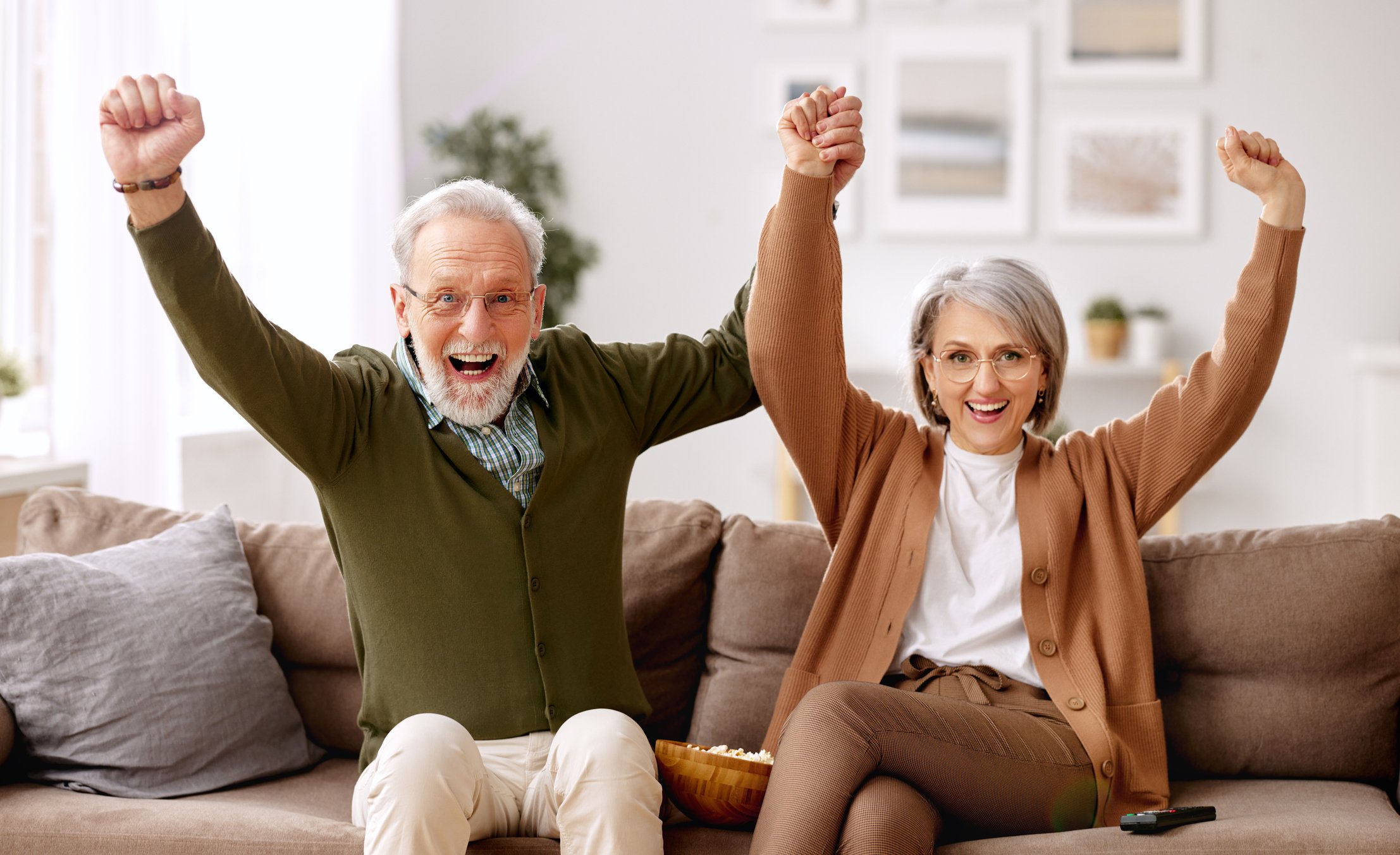 A retired couple pumping their fists and cheering from their couch.