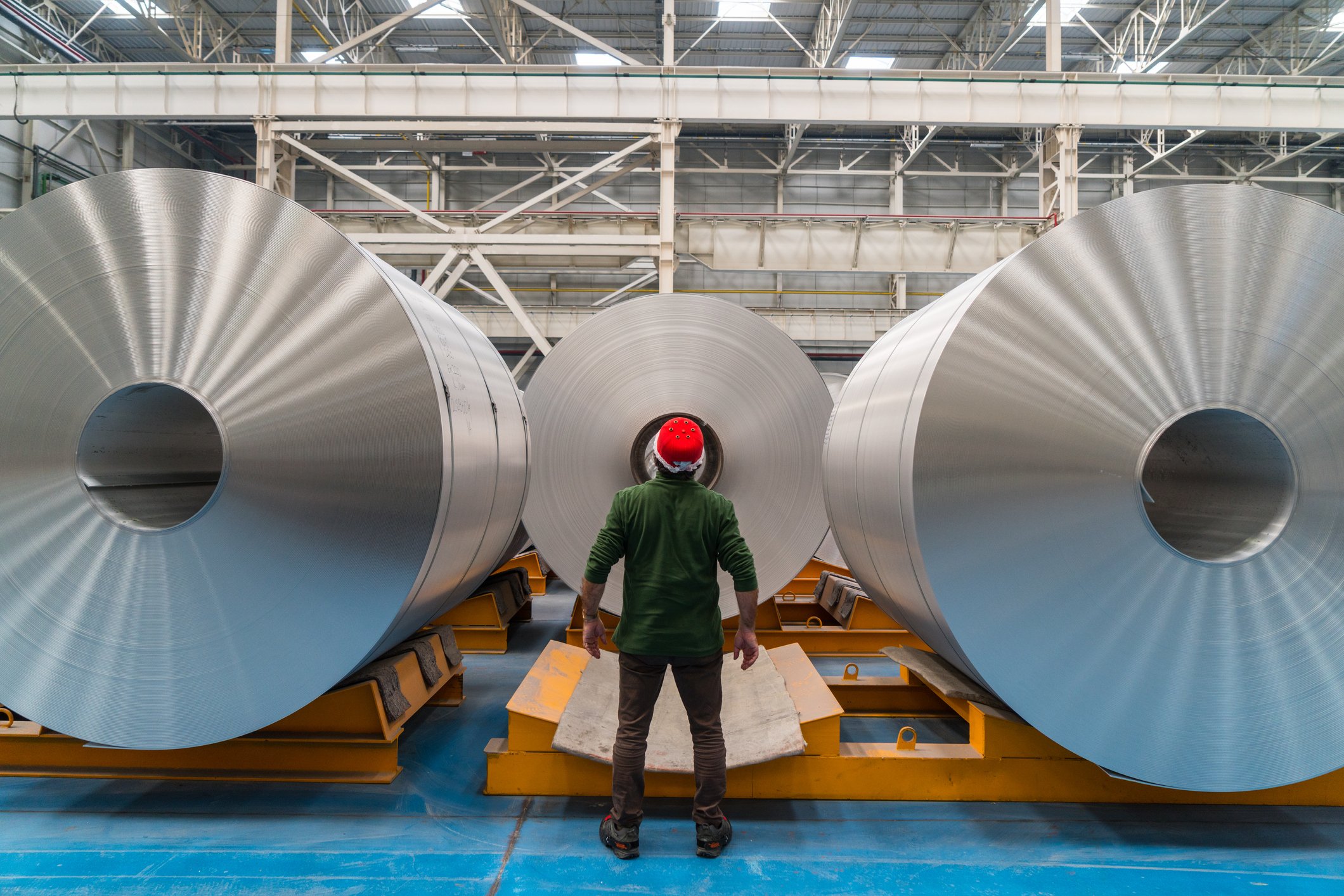 A person standing next to large rolls of aluminum.