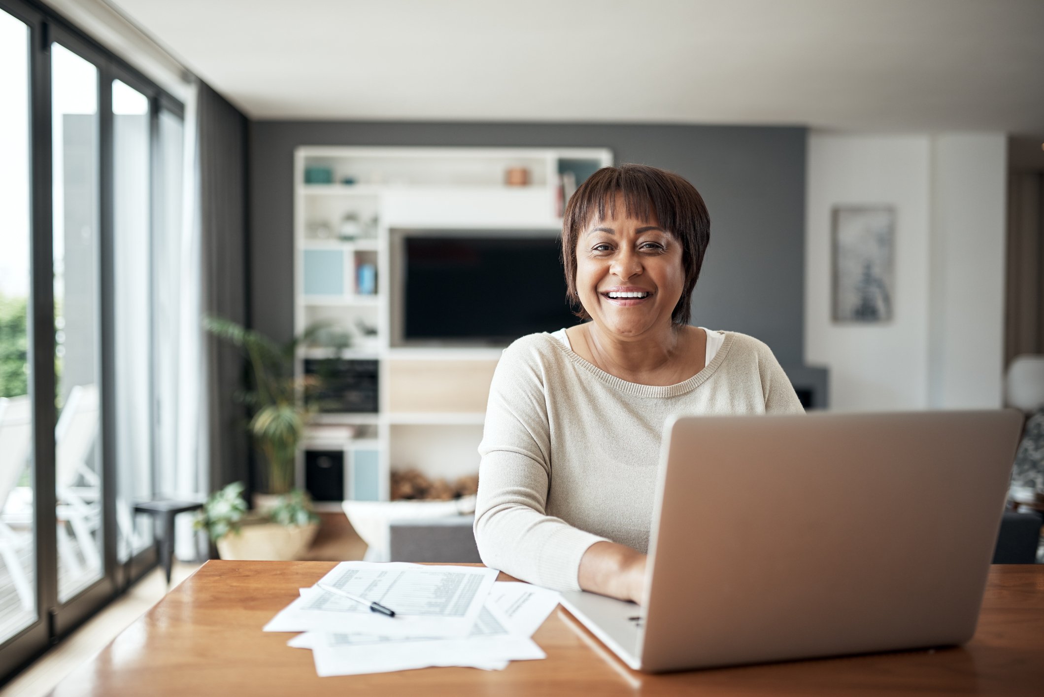 Person smiles while sitting in front of laptop at home with paperwork on the table. 