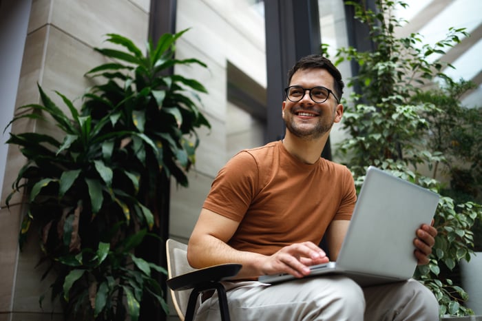 Person smiles while sitting on chair with laptop in outdoor patio.