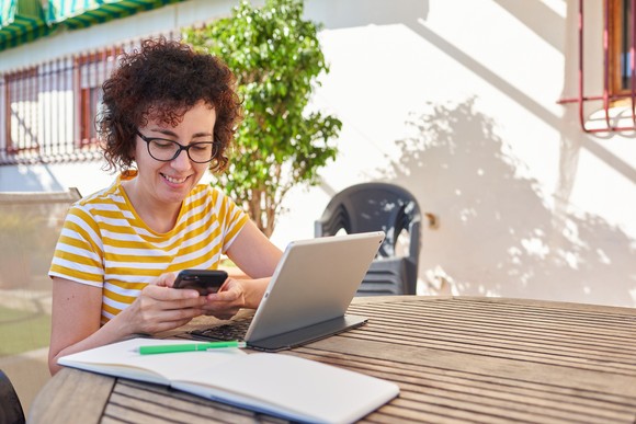 Person working outdoors on a phone and a laptop.