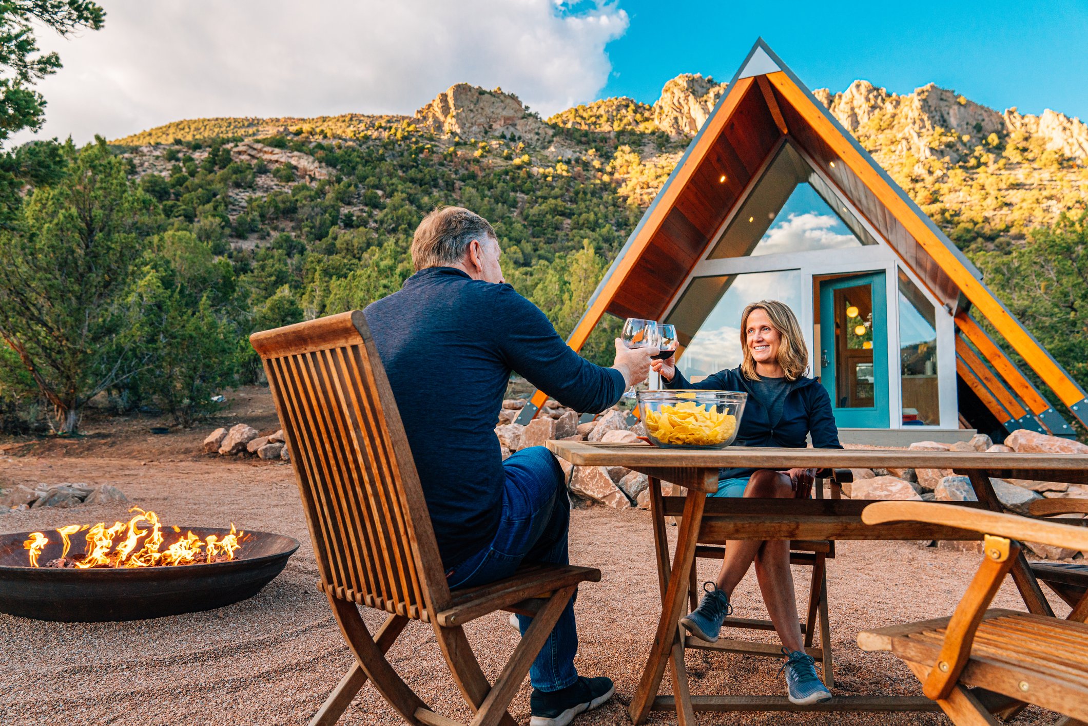 Retired couple enjoying food outdoors near a firepit.