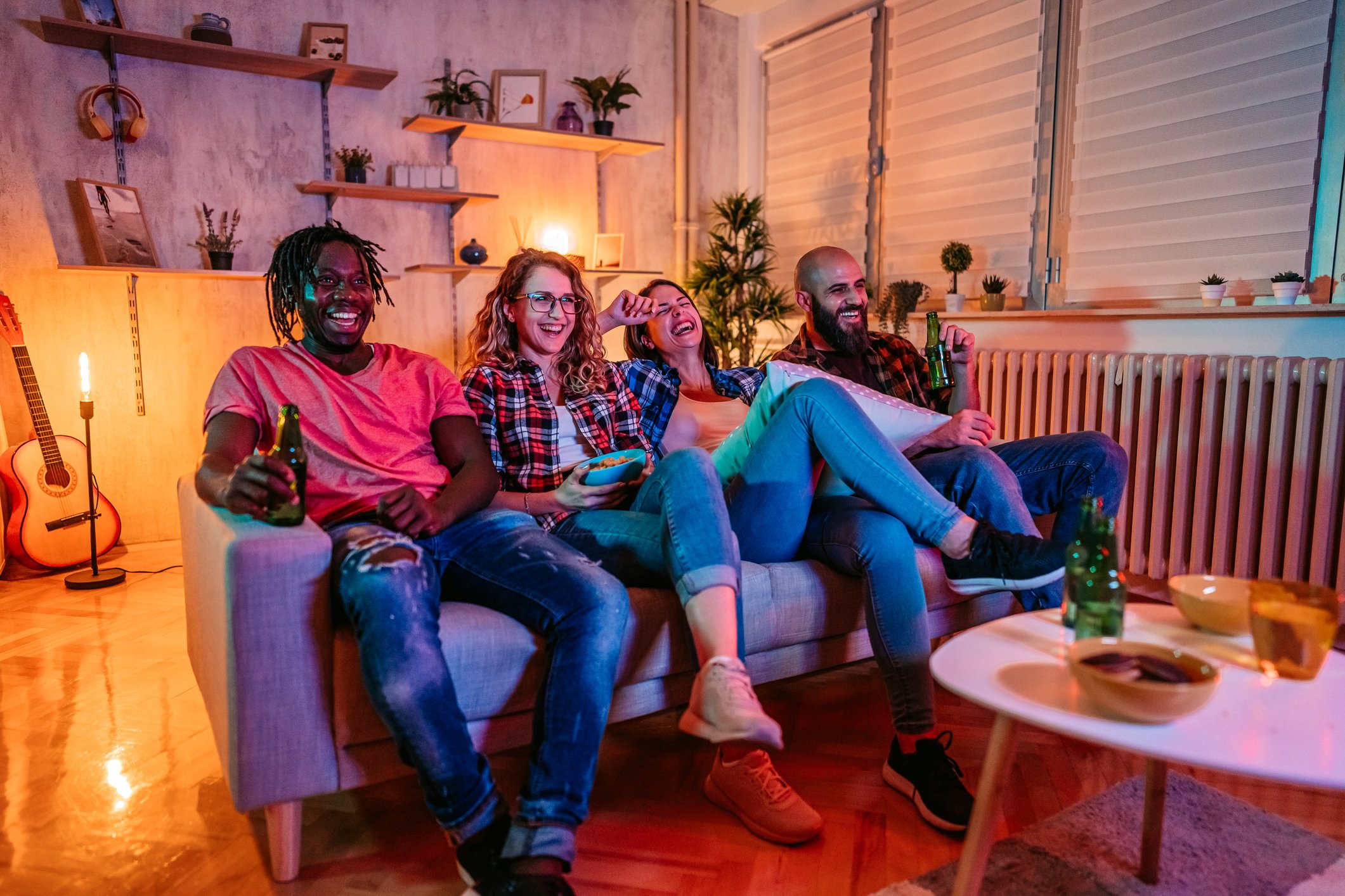 A group of friends sitting on a couch laughing while watching TV.